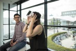 Een student zit in de vensterbank te kijken naar een andere student die een VR bril draagt.